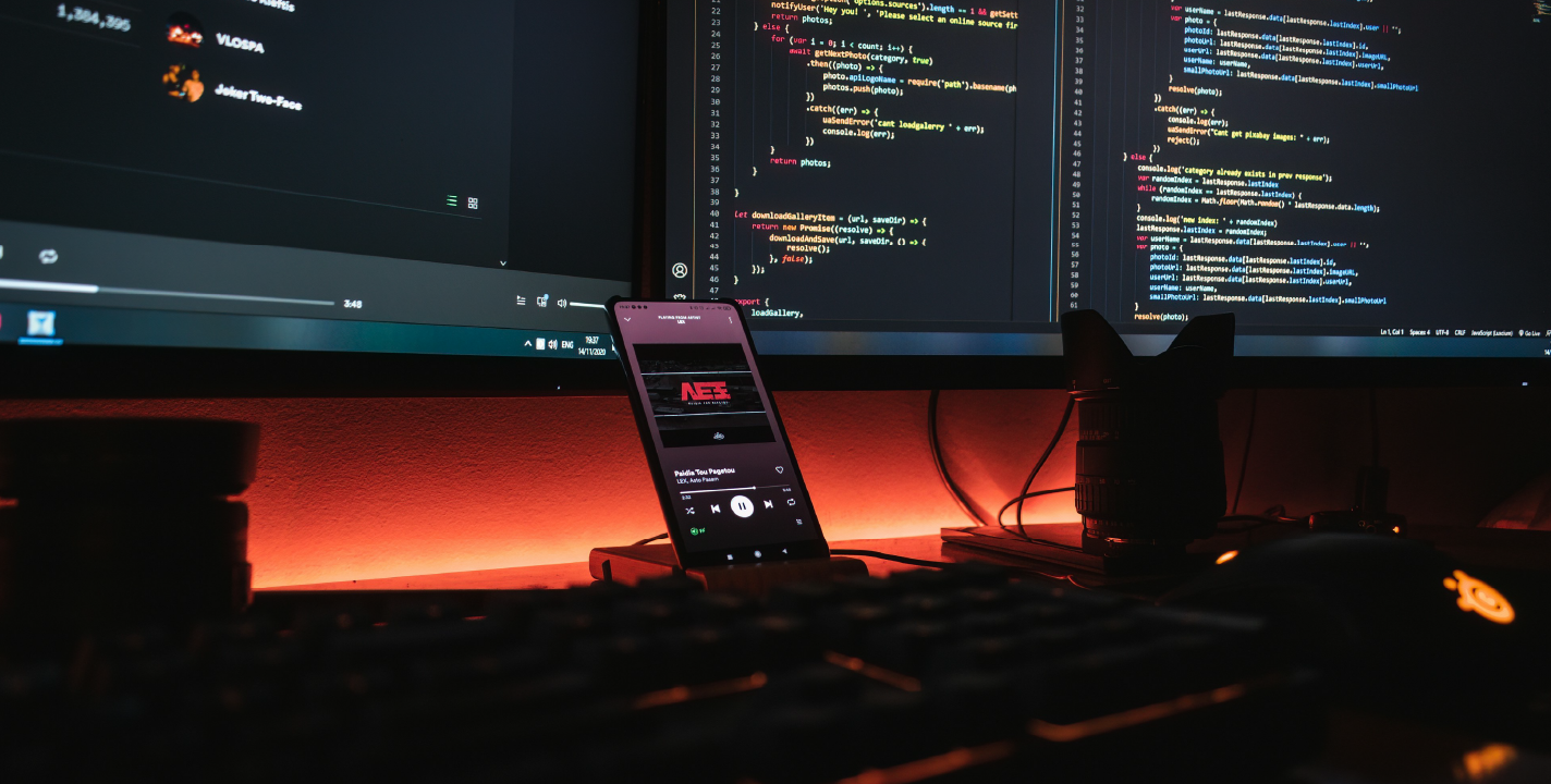 Web application development environment showing dual monitors with code and a smartphone on desk