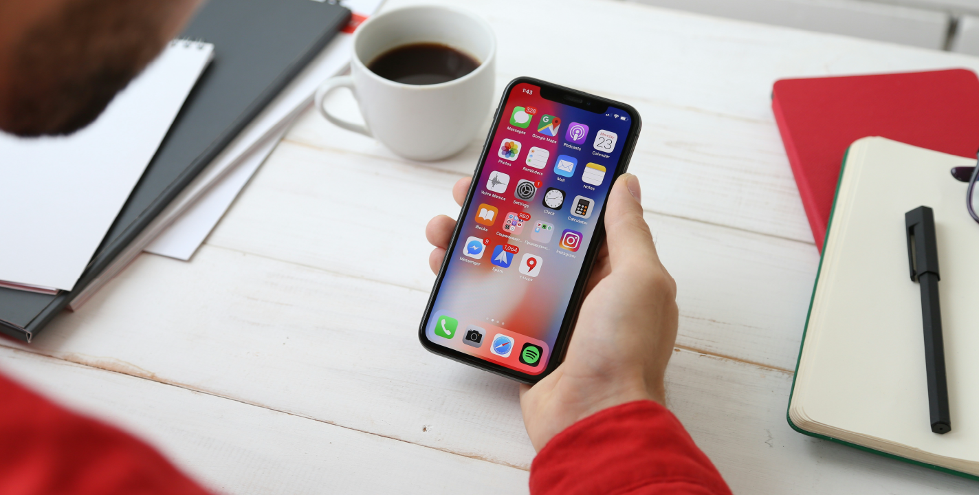 iOS app development setup with person holding iPhone showing home screen apps